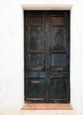Old wooden black double doors with chipped flaking faded peeling paint and rusty handles lock and letterbox in a white painted wal Royalty Free Stock Photo