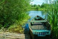 An old wooden boat is moored by the river and the bank overgrown with reeds. Fishing rowing boat in the color of the setting sun. Royalty Free Stock Photo