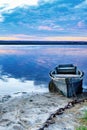 An old wooden boat is moored to the bank with a rusted iron chain on the bank of a calm river against the morning horizon Royalty Free Stock Photo