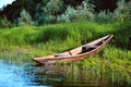 old wooden boat on the river bank close up against the background of green grass and bushes, reflections in the water Royalty Free Stock Photo
