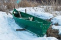 Old wooden boats lie in the snow on the shore of an ice-covered frozen lake in the winter.