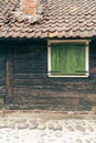 An old wooden building wall with closed green window shutters and red roof tiles, on the side of a stone cobbled street Royalty Free Stock Photo