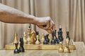 Old wooden chess pieces on chessboard. Hand of adult man making move with white pawn