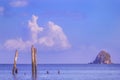 Old wooden columns of the destroyed pier stand in a calm sea in the rays of sunset on the background of the island Royalty Free Stock Photo