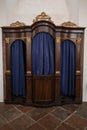 Old wooden confessional with carvings and heavy blue curtains.