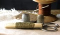 AN OLD WOODEN COTTON REEL WITH BROWN THREAD, DARNING NEEDLE, SCISSORS, THIMBLES AND KHAKI THREAD ON PIECE OF CARDBOARD