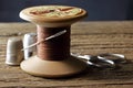 OLD WOODEN COTTON REEL WITH STRONG BROWN COTTON THREAD, A NEEDLE AND THIMBLES AND A PAIR OF SCISSORS IN THE BACKGROUND Royalty Free Stock Photo