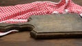 Old wooden cutting board and folded red and white cotton kitchen napkin on a wooden brown background, top view, copy space Royalty Free Stock Photo