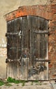 Old wooden dark brown rotten door with wrought iron hinges in a medieval brick wall with remnants of greyplaster Royalty Free Stock Photo