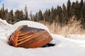 Old wooden destroyed flooded fishing boat lie in snow on shore of ice-covered frozen river in winter, snow in cold morning at Royalty Free Stock Photo