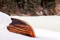 Old wooden destroyed flooded fishing boat lie in snow on shore of ice-covered frozen river in winter, snow in cold morning at Royalty Free Stock Photo