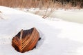 Old wooden destroyed flooded fishing boat lie in snow on shore of ice-covered frozen river in winter, snow in cold morning at Royalty Free Stock Photo