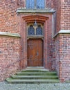 Old wooden door in brick wall with iron fittings, steps and ornamental windows