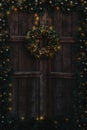 Old wooden door decorated with Christmas garland and wreath, and with warm lights