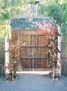 Old wooden door with flowers, chandelier and candles on a stone floor under arch plants Royalty Free Stock Photo