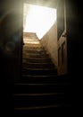 Old wooden door open into basement with light rays shining into dark creepy cellar from stone worn staircase, rundown with shadows