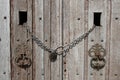 Old wooden doors closed with a chain and a lock. large iron door knockers