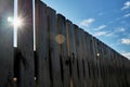 An old wooden fence against a blue sky with clouds on a sunny day. Background of old wooden boards in rustic style Royalty Free Stock Photo