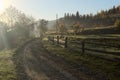 Old wooden fence along the dirt rural road in the early autumn morning Royalty Free Stock Photo