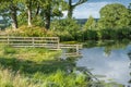 An old wooden fence half submerged into a pretty rural lake with reflections of the fence and surrounding trees