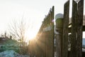 The old wooden fence in the village is covered with snow in winter. The rays of the rising sun shine through the fence boards Royalty Free Stock Photo