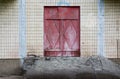 Old wooden fire door painted with red paint on a background of an old white tiles of an old house Royalty Free Stock Photo