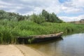 Old wooden fisherman boat on the river. Beautiful summer landscape with high reeds on the shore, lake and sky with clouds. Retro Royalty Free Stock Photo