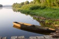 Old wooden fishing boat anchored by the green bank of the river next to the old wooden pier, copyspace Royalty Free Stock Photo