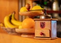 An old wooden hand coffee grinder in front of a fruit bowl.