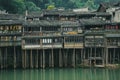 Old wooden hanging houses on the picturesque Tuojiang River in the historic Chinese city of Fenghuang.