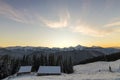 Old wooden house, hut and barn in deep snow on mountain valley, spruce forest, woody hills on clear blue sky at sunrise copy space Royalty Free Stock Photo