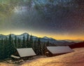 Old wooden house, hut and barn, pile of firewood in deep snow on mountain valley, spruce forest, woody hills on dark starry sky Royalty Free Stock Photo