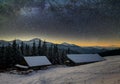 Old wooden house, hut and barn, pile of firewood in deep snow on mountain valley, spruce forest, woody hills on dark starry sky Royalty Free Stock Photo