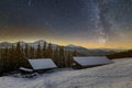 Old wooden house, hut and barn, pile of firewood in deep snow on mountain valley, spruce forest, woody hills on dark starry sky Royalty Free Stock Photo