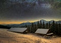 Old wooden house, hut and barn, pile of firewood in deep snow on mountain valley, spruce forest, woody hills on dark starry sky Royalty Free Stock Photo