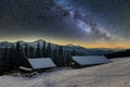 Old wooden house, hut and barn, pile of firewood in deep snow on mountain valley, spruce forest, woody hills on dark starry sky Royalty Free Stock Photo