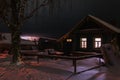 Old wooden house in a village with big trees and snowdrifts. Rural view in winter at night Royalty Free Stock Photo