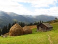 Old wooden hut and haystacks on background of beautiful mountain landscape and clouds. Royalty Free Stock Photo