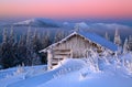 Old wooden hut. Huge snowdrifts around. Background of the high mountains. High fairtrees freezed with snowflakes.