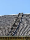 Old wooden ladder on slate roof with blue sky in background