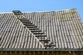 Old wooden ladder on slate roof with blue sky in background