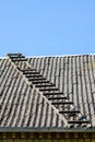 Old wooden ladder on slate roof with blue sky in background