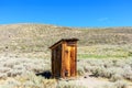 Old wooden outhouse in Bodie State Historic Park. Scenic rolling hills covered with sagebrush under blue sky