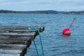 An old, wooden pier with a blue rope. Red anchoring bouy in the sea in the background Royalty Free Stock Photo