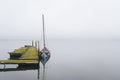 An old wooden pier and a brightly painted fishing boat next to it on the background of a foggy Atlantic ocean bay Royalty Free Stock Photo