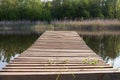 Old wooden pier above a calm reflective river, surrounded by bright spring greenery and peaceful nature. Royalty Free Stock Photo