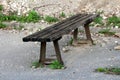 Old wooden public bench with strong rusted metal supports mounted on paved edge of abandoned parking place surrounded with rocks