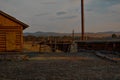 Old wooden Russian house with fence, barn with closed shutters in red warm light of sunset, with shadows on dry grass. Abandoned Royalty Free Stock Photo