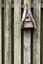 Old, wooden, and rustic bird feeder hanging on a fence in a backyard garden. Closeup of a vintage birdhouse on a wall