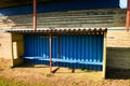 Old wooden seats on outdoor stadium players bench, chairs with worn paint below rusty metal sheets roof. Autumn poor grass Royalty Free Stock Photo